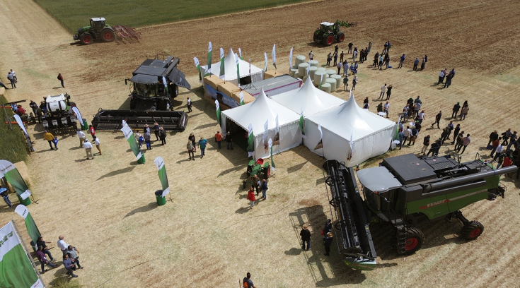 Zelte mit Fendt Mähdreschern und Traktoren rundherum auf einem Feld