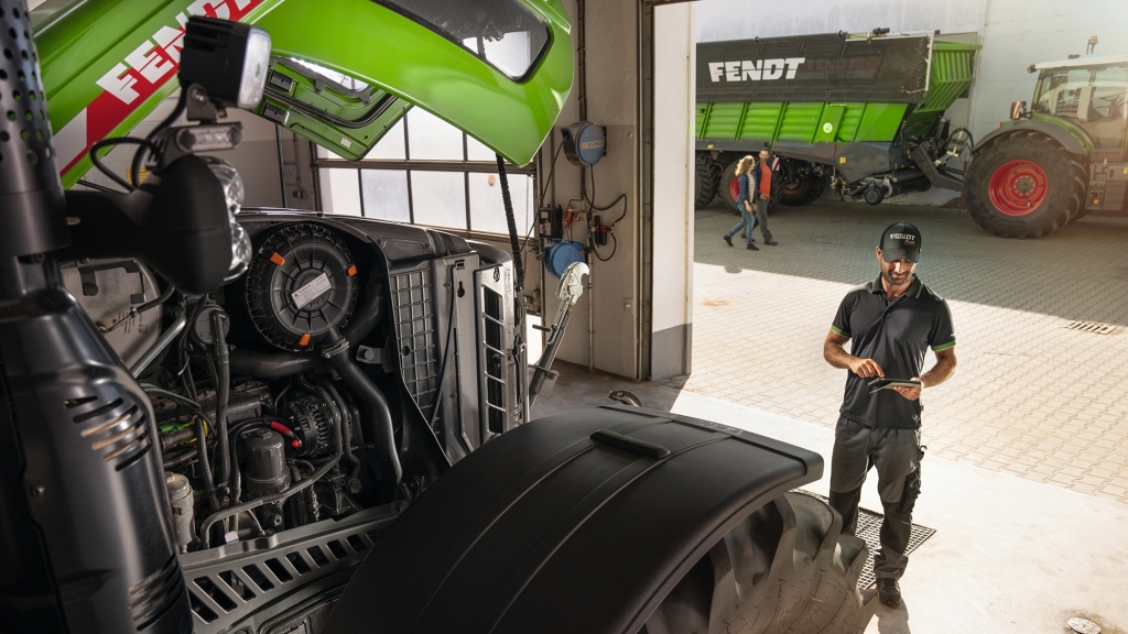 Ein Servicemitarbeiter in der Fendt Händler Werkstatt mit Kunden im Hintergrund