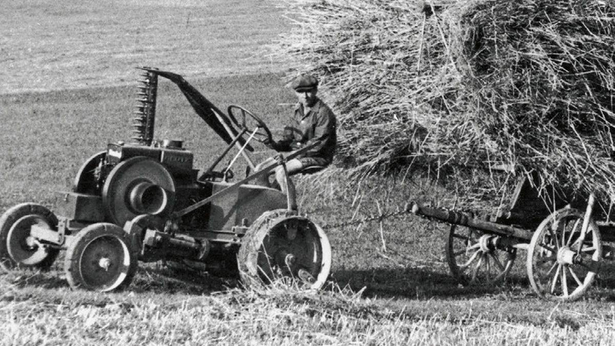 Schwarz-Weiß-Aufnahme wie ein Landwirt mit einem Dieselross auf einer Wiese färht