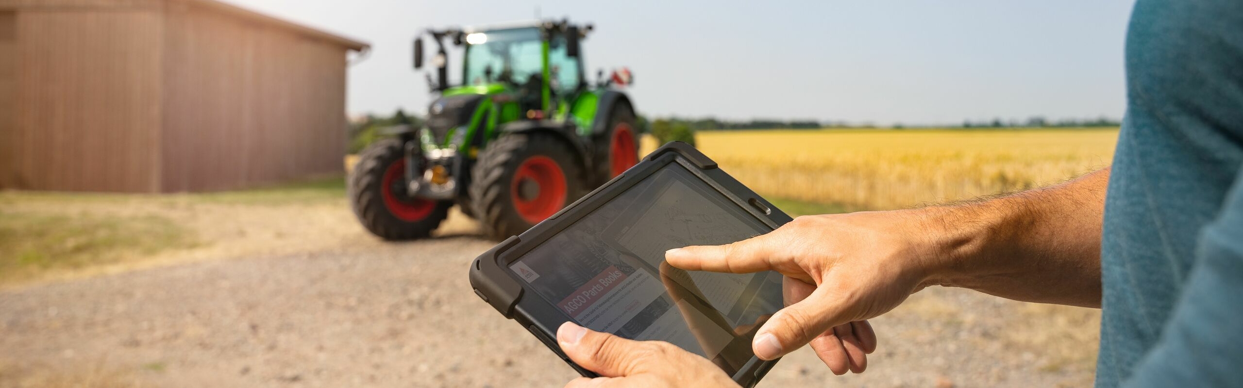 Ein Landwirt verwendet auf seinem Tablet eine Fendt Service App, im Hintergrund sein grüner Fendt 700 Vario