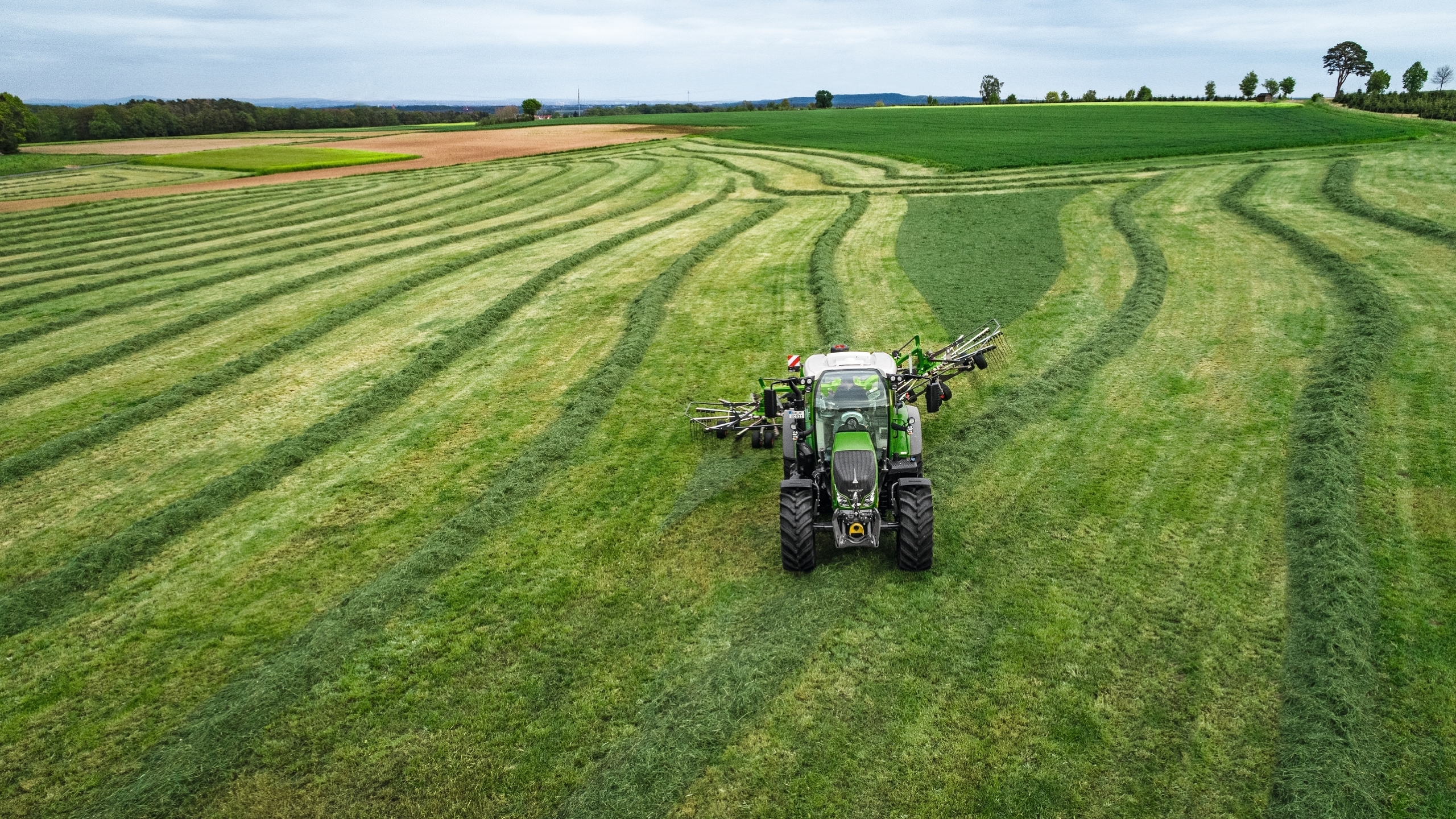 Ein Fendt Traktor fährt mit einem Fendt Schwader auf dem Feld.