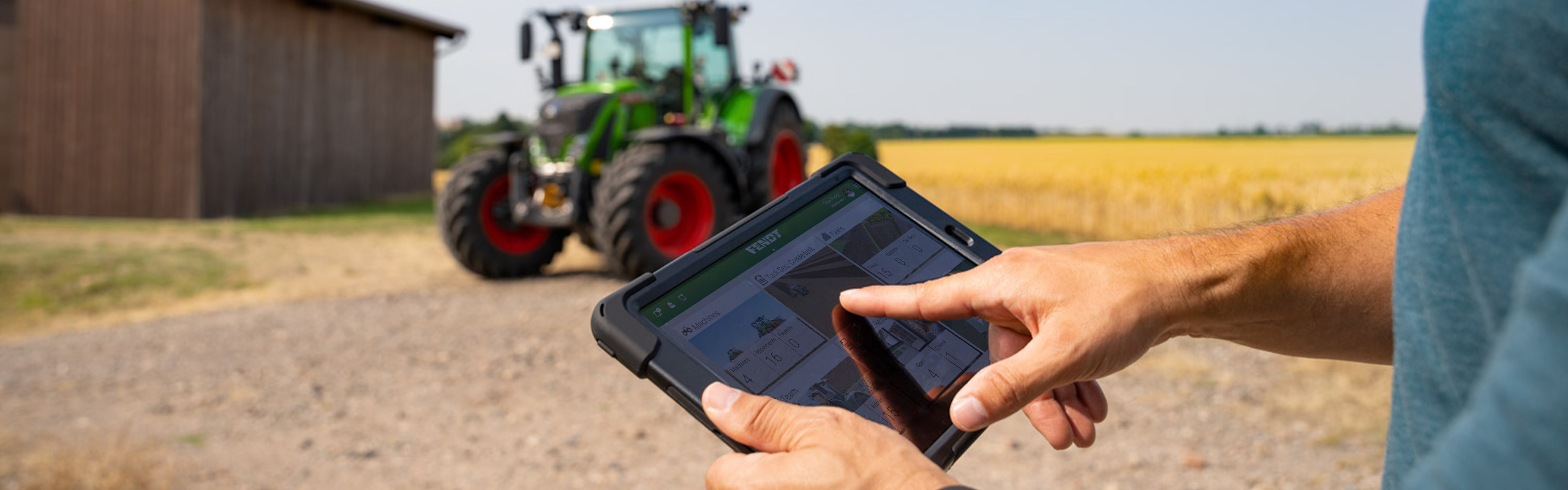 Ein Landwirt hält ein Tablet, auf dem FendtONE offboard geöffnet ist, in der Hand. Im Hintergrund steht ein Traktor.