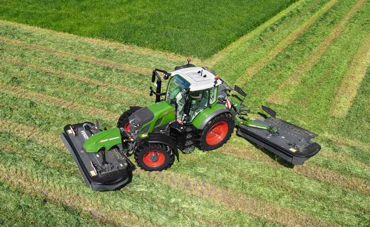 Ein Fendt Traktor mit einem Fendt Mähwerk steht auf einer grünen Wiese, die bereits zum Teil abgemäht wurde