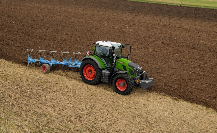 Ein Fendt Traktor pflügt ein Feld mit einem blauen Pflug.