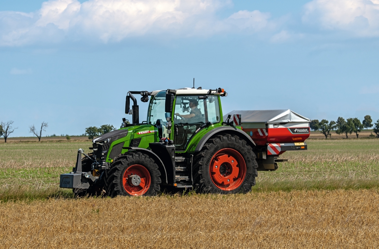 Ein Fendt Traktor fährt mit einem Kunstdüngerstreuer fährt über einen Acker mit Getreide