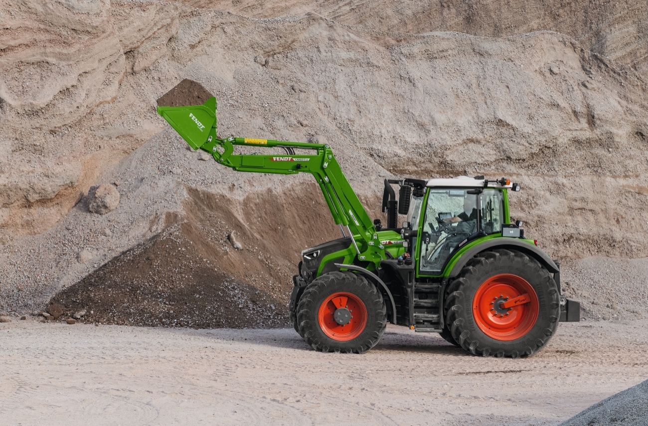 Ein Fendt Traktor mit Frontladerschaufel. Im Hintergrund ist ein Berg aus Kies und Sand.