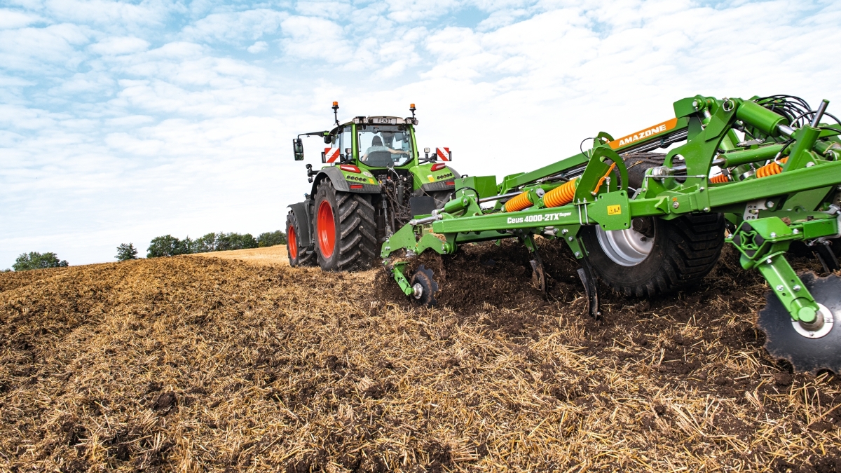 Eine Landwirtin fährt mit einem Fendt 700 Vario Gen7 und einem Amazone Grubber auf dem Acker.