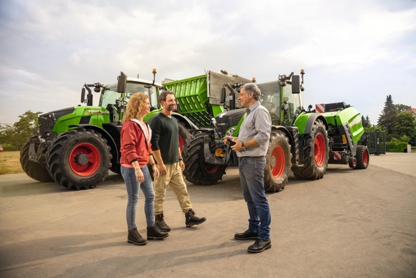 Ein Landwirt und eine Ladnwirt stehen mit einem Händler vor zwei Traktoren und bereiten sich auf die Testfahrt vor.