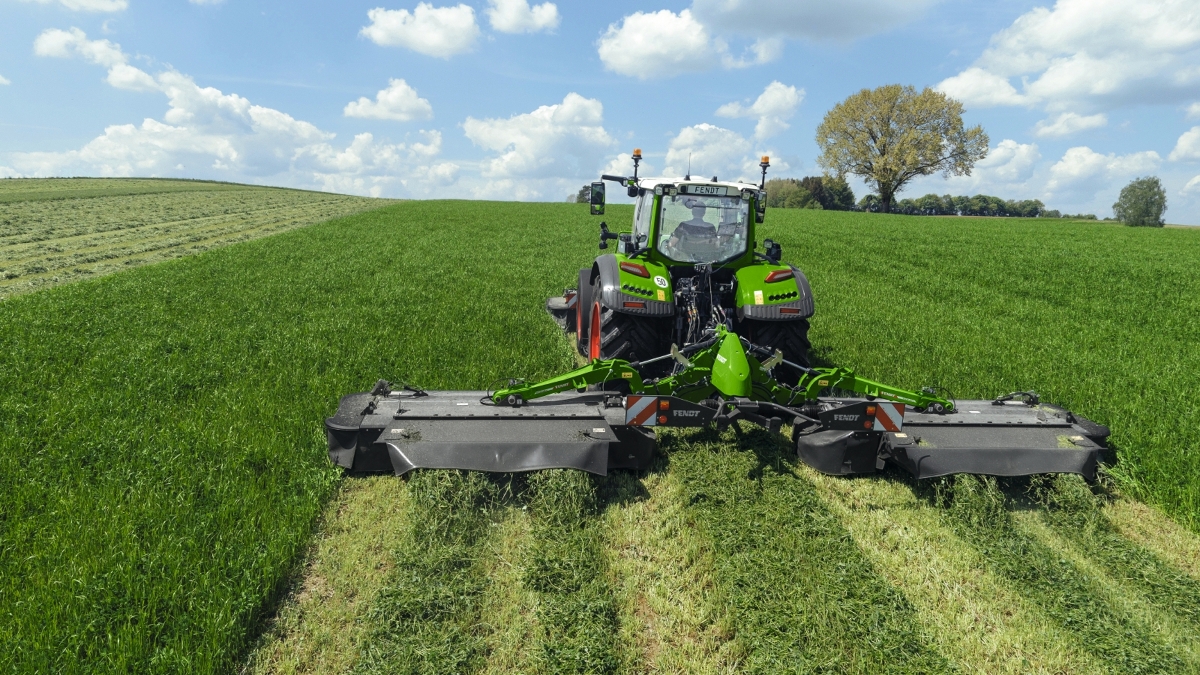 Ein grüner Fendt Traktor im Grünland mit angehängter Slicer 860 KC Mähkombination