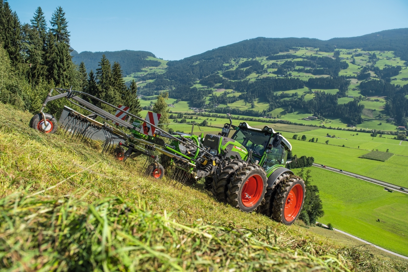 Fendt 200 Vario Traktor mit Zwillingsbereifung und Frontschwader auf Wiese in Hanglage