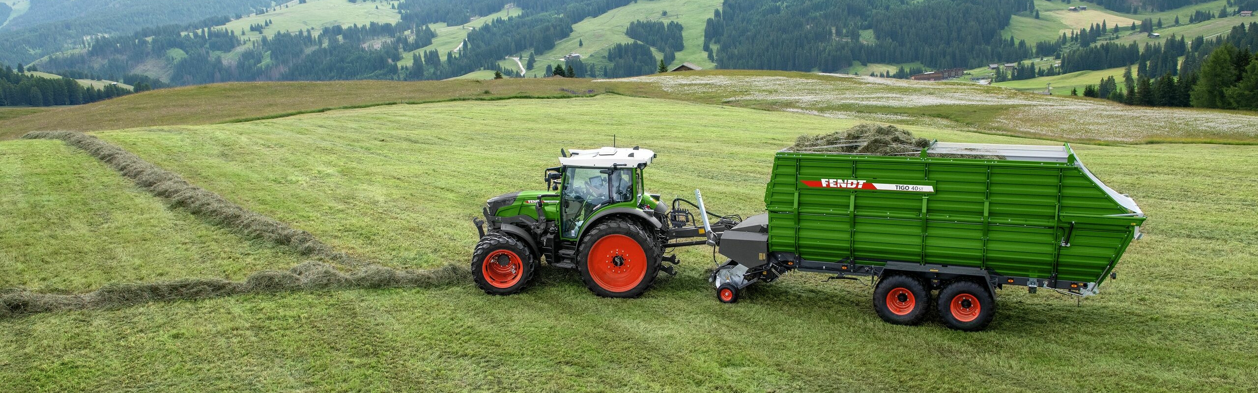 Ein grün lackierter Fendt 200 Vario mit angehängtem Tigo Ladewagen im alpinen Einsatz