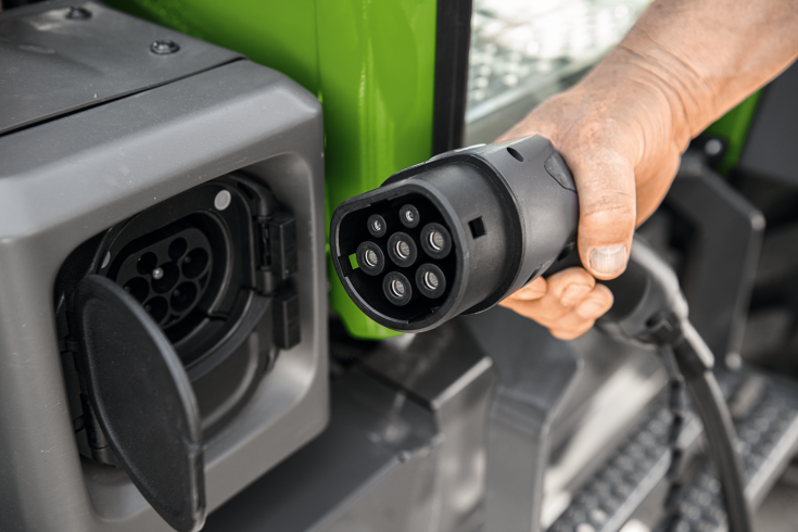 Ladebuchse Fendt e100 Vario Eine männliche Hand hält den Stecker des Ladekabels für den Fendt e100 Vario, daneben die offene Ladebuchse am Traktor