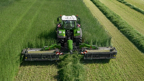Fendt Slicer 960 KCB Pro Ein Fendt Traktor mit Fendt Slicer Mähwerk auf einer grünen Wiese aus der Vogelperspektive.
