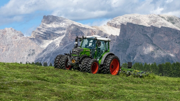 Ein grün lackierter Fendt 200 Vario mit angehängtem Fendt Alpin-Wender im Alpin-Einsatz vor massiver Bergkulisse.