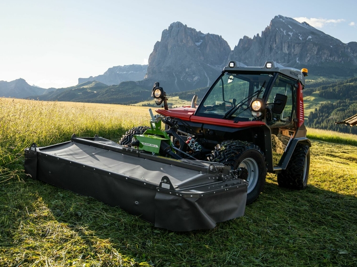Das Mähwerk Fendt Slicer Alpin im Einsatz auf einer Bergwiese mit Bergen und blauem Himmel im Hintergrund