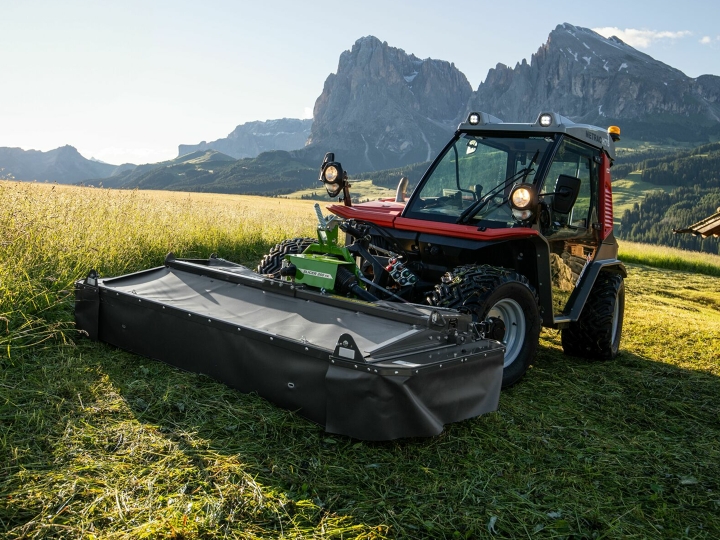Das Mähwerk Fendt Slicer Alpin im Einsatz auf einer Bergwiese mit Bergen und blauem Himmel im Hintergrund