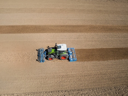 Ein grün lackierter Fendt mit roten Felgen fährt auf einem abgeernteten Feld und bearbeitet den Boden