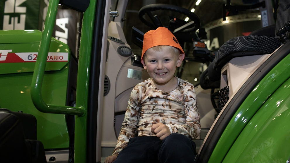 Kind sitzt auf Fendt Traktor Ein kleiner Junge sitzt auf der Treppe eines Fendt Traktors, lächelt fröhlich und trägt eine orange Mütze