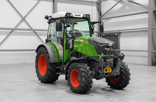 Der grüne Fendt mit den roten Felgen steht in einer Halle mit grauem Boden.
