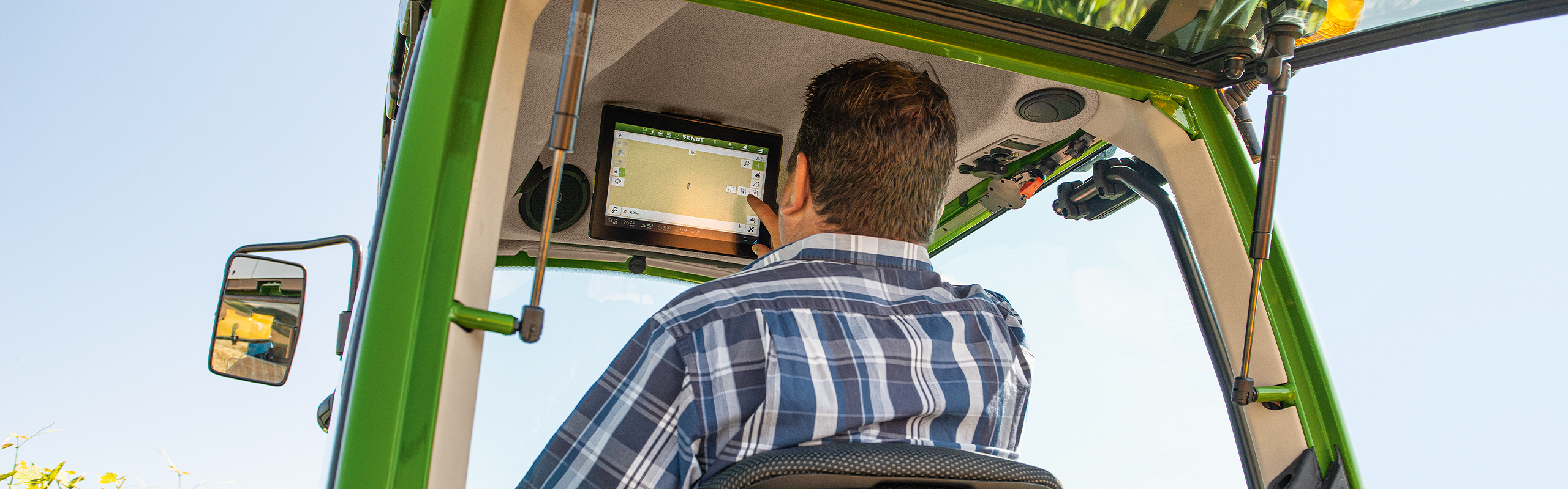 Ein Mann sitzt in der Kabine des Fendt 200 V/F7P Vario und tippt mit dem Finger auf dem Terminal über der Frontscheibe herum.