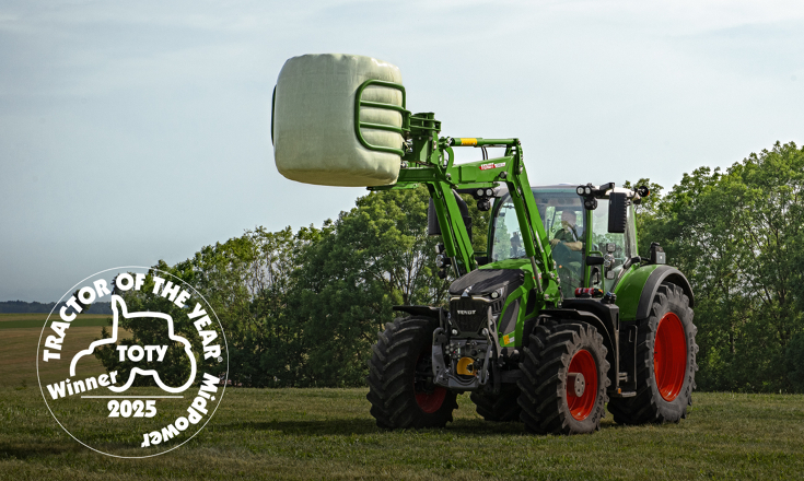 Fendt 620 Vario mit angehobenem Fendt Frontlader mitTractor of the Year 2025 Logo Fendt 620 Vario mit angehobenem Fendt Frontlader auf einer Wieser mit einem Rundballen in der Ballenzange - vorne links ist das Logo desractors of the Year in der Kategorie MidPower in weiß platziert