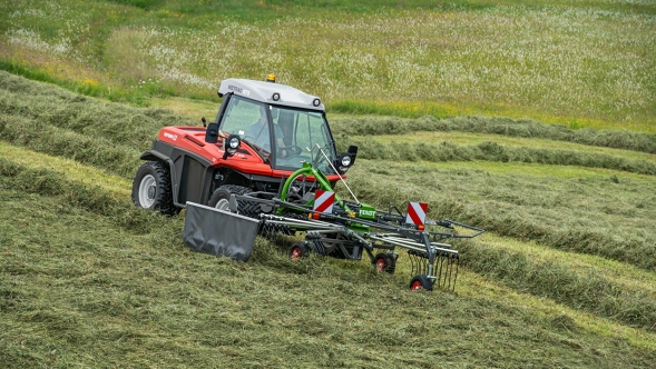 Grüner Fendt Former im Einsatz auf einer Bergwiese, im Hintergrund sind bereits die hinterlassenen Schwadspuren zu sehen.