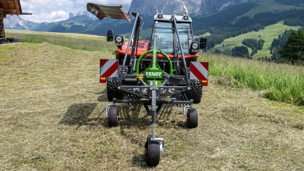 Der grüne Fendt Alpin Einkreiselschwader steht auf einer Bergwiese mit einer Berglandschaft im Hintergrund.
