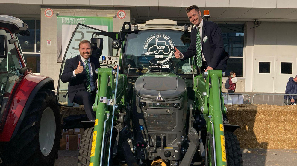 2 italienische Fendt Mitarbeiter mit einem Fendt e100 Vario samt TotY 2025 Logo auf der Frontscheibe freuen sich 2 italienische Fendt Mitarbeiter sitzen links und rechts auf dem Fendt e100 Vario samt TotY 2025 Logo auf der Frontscheibe und freuen sich