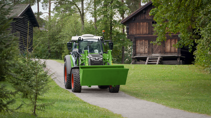 Fendt e100 Vario in Norwegen Fendt e100 Vario fährt mit einer Schaufelin Norwegen af einer Straße,zwei Holzhäuser im Hintergrund