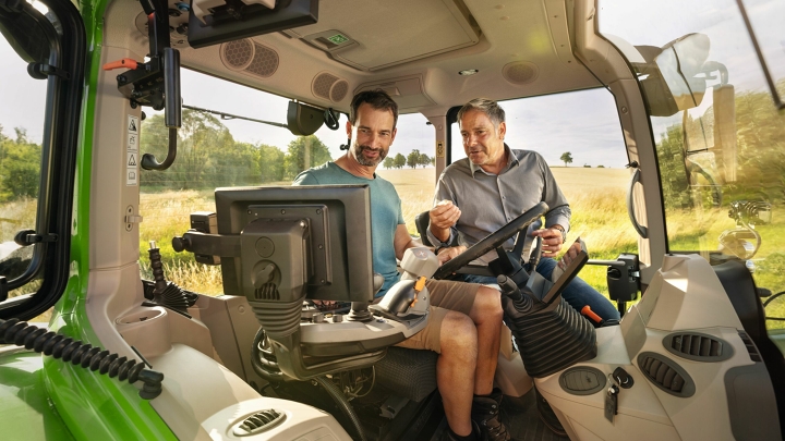 Ein Fendt Händler in der Kabine eines grünen Traktor-Vorführmodells von Fendt bei einem Landwirtskunden auf dem Gelände