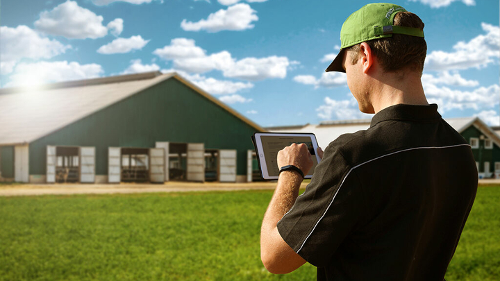 Ein Landwirt steht mit Tablet in der Hand vor seinem Hof und meldet sich für den Fendt Newsletter an