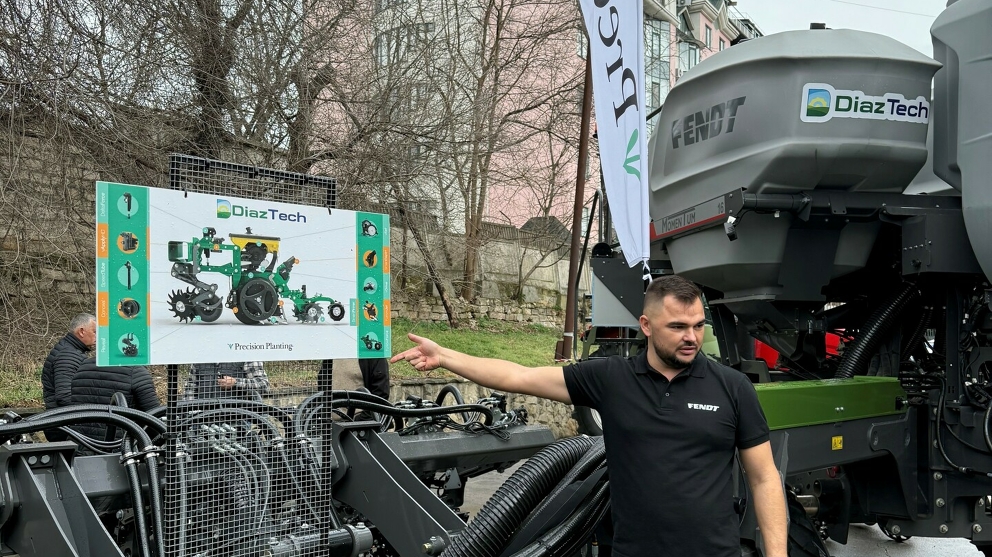 Roman Braguta, Produkt Manager DiazTech auf der Messe Moldagrotech 2025 Ein Mann mit schwarzem T-shirt zeigt auf ein Schild, das Schild zeigt ein Zeichnung einer Sämaschine