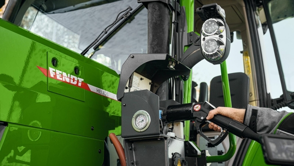 Nahaufnahme eines grünen Fendt-Traktors beim Tanken mit Wasserstoff. Der Zapfhahn steckt im Tankstutzen, daneben sind ein Messgerät und Maschinenteile zu sehen.