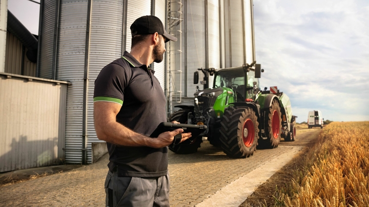 Ein Fendt Service-Techniker schaut auf einen Fendt Traktor 700 Vario Gen6 am Feldrand