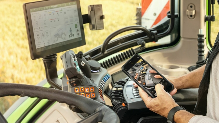 Ein Landwirt sitzt in einem Traktor und schaut auf seinem Handy ein Erklärvideo an.