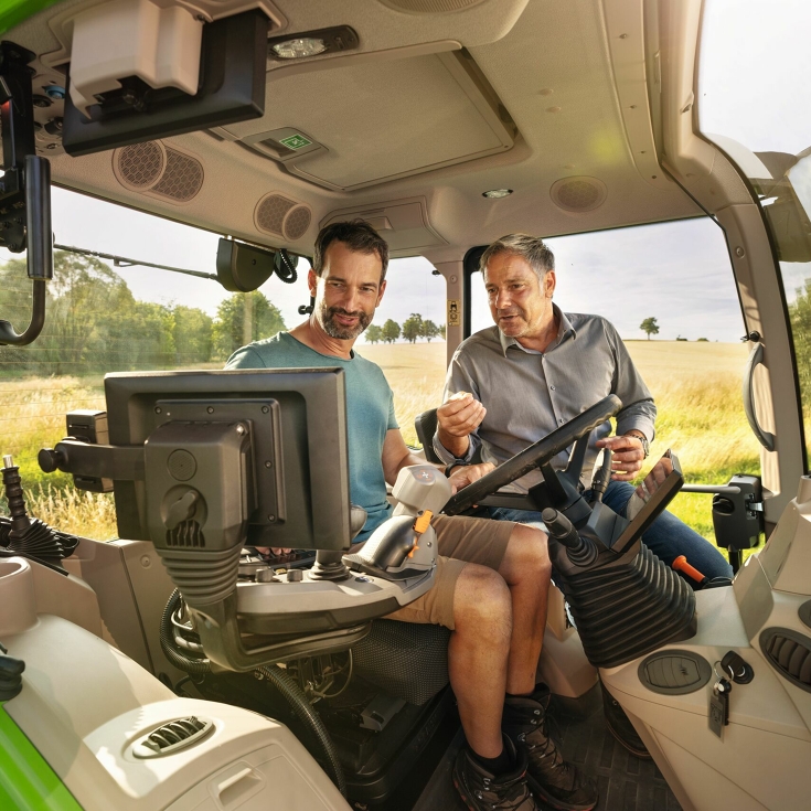 Ein Landwirt fährt mit einem Fendt Traktor und bekommt von Händler gezeigt, wie die Maschine funktioniert.