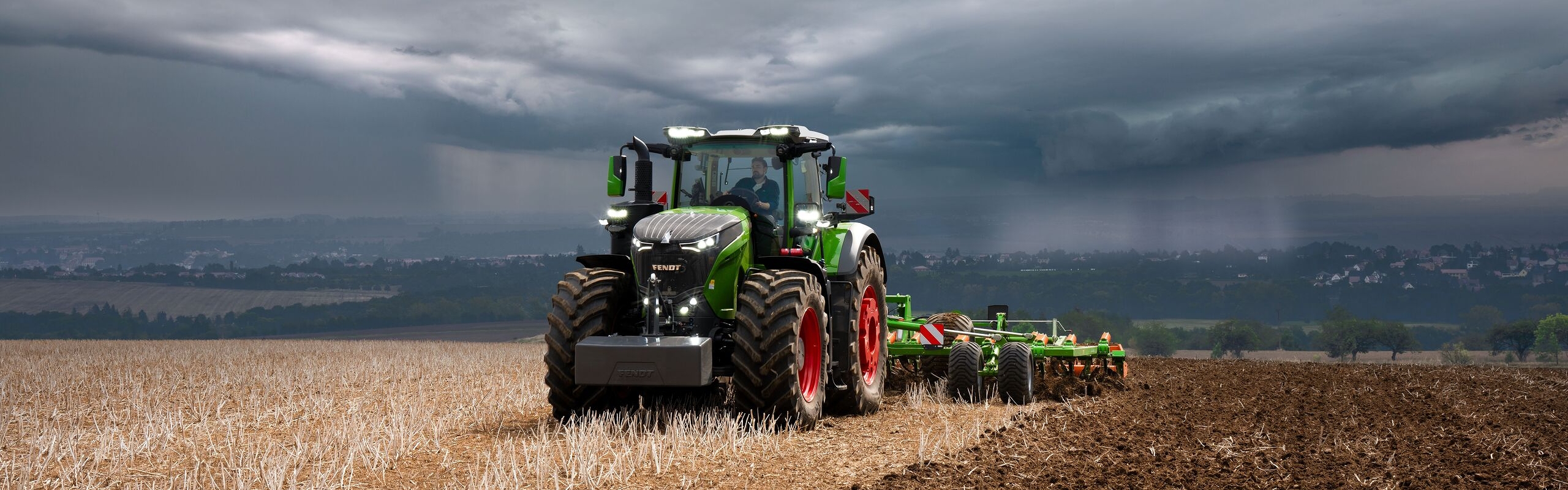 Vor schweren, heraufziehenden Gewitterwolken in der Ferne erledigt der Fendt 1000 Vario Traktor noch kraftvoll seine Feldarbeit