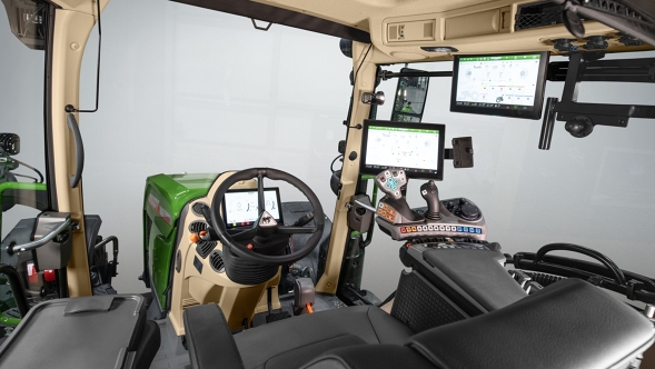 Innenansicht der Kabine eines Fendt 500 Vario Gen4 Traktors mit beigem Dachhimmel, schwarzem Fahrersitz und mehreren digitalen Displays. Rechts neben dem Lenkrad befinden sich ein großes Terminal, ein Joystick und ein Armaturenfeld mit bunten Tasten. Oben ist ein weiterer Monitor montiert. Die Kabine wirkt hell, aufgeräumt und modern.