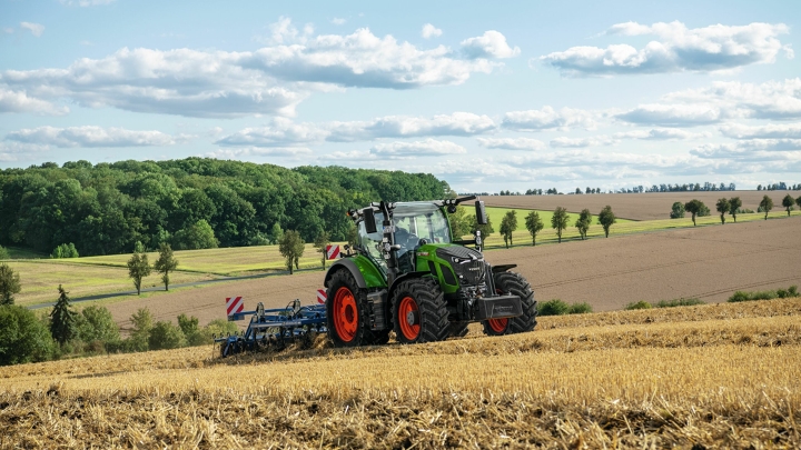 Ein grüner Fendt Traktor mit roten Felgen bei der Bodenbearbeitung auf einem abgeernteten Feld mit sanfter Hügellandschaft im Hintergrund