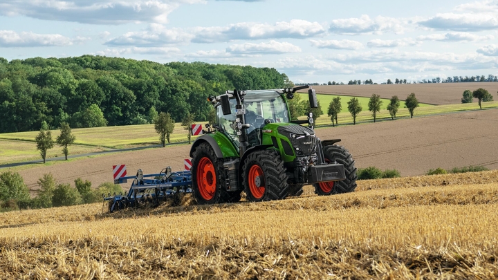 Ein grüner Fendt Traktor mit roten Felgen bei der Bodenbearbeitung auf einem abgeernteten Feld mit sanfter Hügellandschaft im Hintergrund