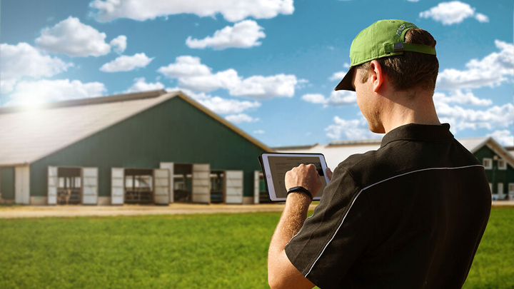 Ein Landwirt steht mit Tablet in der Hand vor seinem Hof und meldet sich für den Fendt Newsletter an