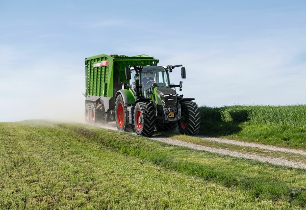 Fendt 600 Vario Der grüne Fendt 600 Vario Traktor mit roten Felgen und dem grünen Ladewagen Fendt Tigo fährt auf einer kleinen Feldstraße mit einer grünen Wiese im Vorder- und Hintergrund.