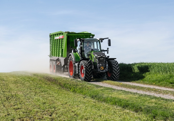 Fendt 600 Vario Der grüne Fendt 600 Vario Traktor mit roten Felgen und dem grünen Ladewagen Fendt Tigo fährt auf einer kleinen Feldstraße mit einer grünen Wiese im Vorder- und Hintergrund.