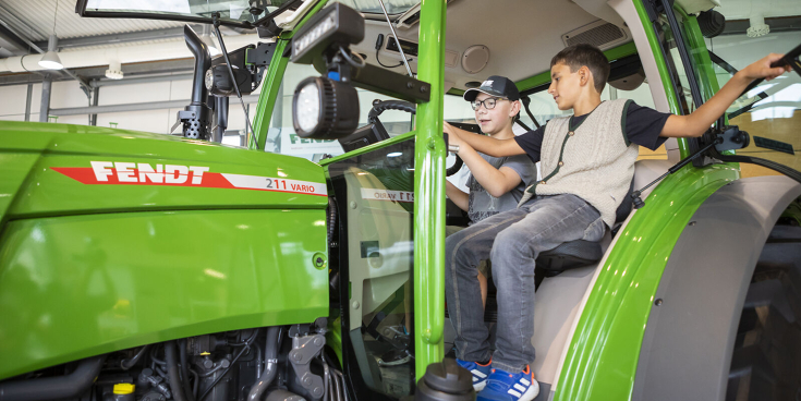 Willkommen zu den Fendt Holiday Weeks Zwei Jungs sitzen gemeinsam in einem Fendt Traktor 200 Vario im Fendt Forum