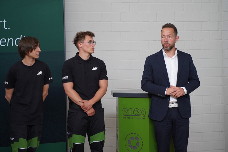 (v.l.) Danny Hentschel (Auszubildender), Yannik Richter (Auszubildender) und Alexander Schenk (Leiter des Standortes Hohenmölsen) 2 Azubis und ein weiterer Mann stehen vor einer weißen Wand, die beiden Azubis schauen den Mann im Anzug an während dieser spricht