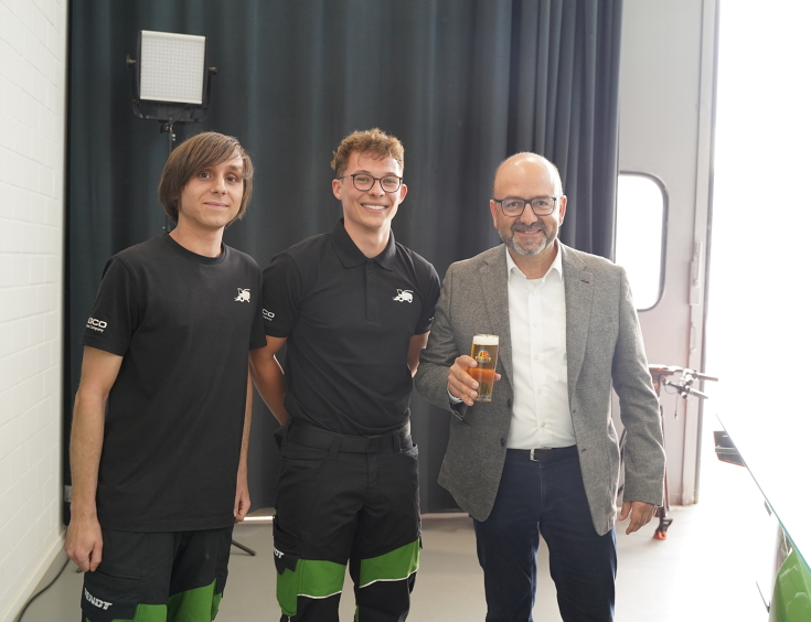 3 Männer, 2 davon sind Azubis (links), der Mann rechts trinkt ein gezapftes Kaltgetränk