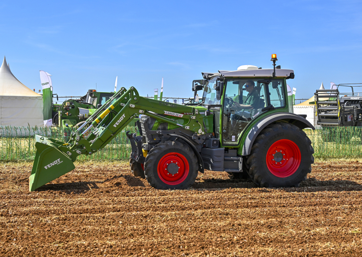 grüner Fendt e100 Vario mit Frontlader auf einem Feld im Hintergrund ein Zelt