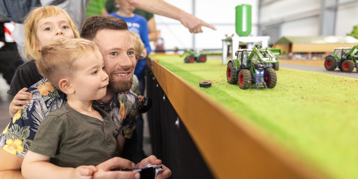 Mann spielt mit Kind im Arm mit einem ferngesteuerten Fendt-Traktor