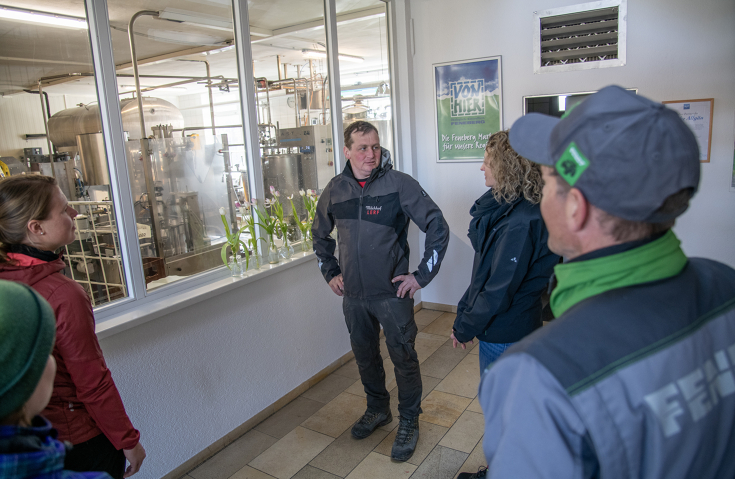 Landwirt Michael Lerf in einer Unterhaltung mit Fendt Mitarbeitenden Menschen in einem Raum. In der Mitte des Fotos steht ein Mann, der eine Frau ansieht und ihr zuhört. Die Frau ist nur seitlich zu sehen. Um die beiden herum stehen weitere Menschen und schauen sie an.