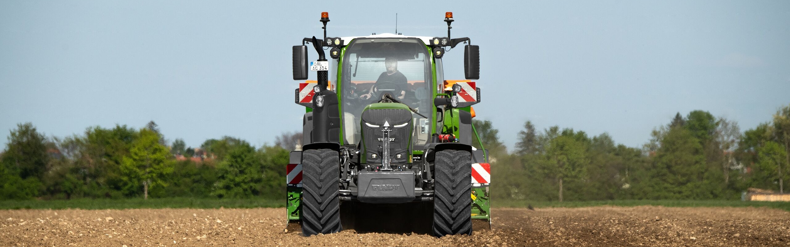 Ein Fendt 300 Vario Gen5 Traktor fährt frontal auf den Betrachter zu und bearbeitet den Boden auf einem Acker unter freiem Himmel